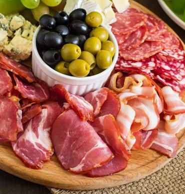 piatto-di-antipasto-con-pancetta-scatti-salame-formaggio-e-uva-su-un-tavolo-di-legno Antipasto catering platter with bacon, jerky, salami, cheese and grapes on a wooden background